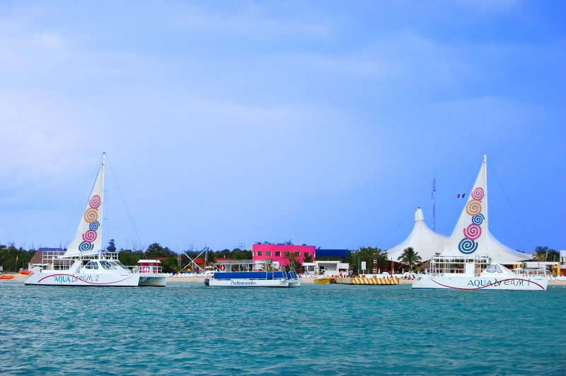 Two Aqua Dream catamarans moored at the colorful Playa Mia beach club with white tent pavilions in Cozumel