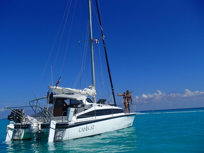 Small 32ft sailing catamaran under sail in turquoise Caribbean waters heading toward Belize cayes