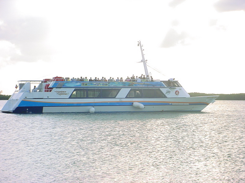 El barco Discovery lleno de invitados en su cubierta superior abierta navegando la laguna tranquila de Cancún a contraluz