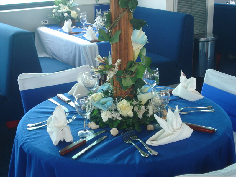 Acercamiento de una mesa de boda del Discovery con mantel azul, centro de alcatraces, copas de vino y servilletas dobladas