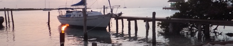Velero amarrado al atardecer junto al muelle de madera del restaurante Sunset Grill en Isla Mujeres, con antorcha encendida sobre la laguna turquesa en calma