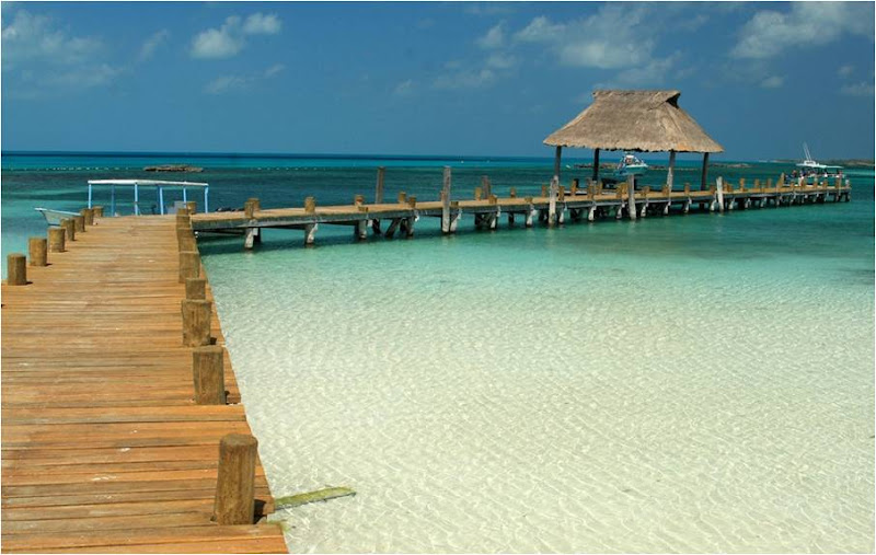 Long wooden pier with a thatched palapa stretching over the calm white-sand shallows of Isla Contoy near Cancun