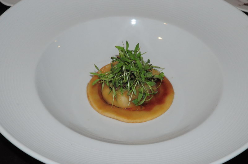 Pasta rellena coronada con brotes verdes y una salsa brillante en un plato hondo blanco, una entrada gourmet del banquete de Maroma