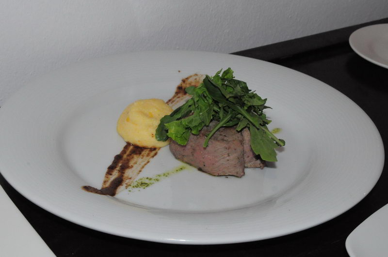 Lomo asado en rebanadas con puré de papa al azafrán y arúgula fresca en un plato blanco, un plato fuerte del servicio de banquetes de Maroma