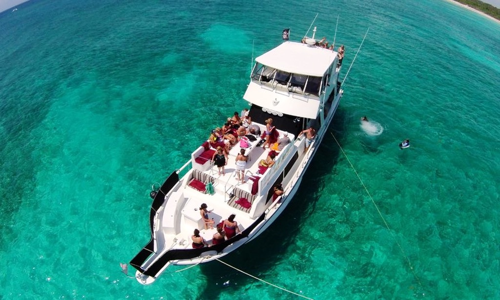 A large white motor yacht / trawler with an enclosed flybridge moored alongside a stone quay, with a thatched palapa and tropical greenery behind it and calm greenish marina water in the foreground.
