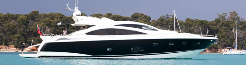 Mega yate Sunseeker Manhattan 64 de casco oscuro anclado en aguas turquesa cristalinas del Caribe frente a una costa verde cerca de Cancún