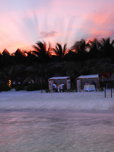 Romantic candle-lit cabana dinners on Maroma beach beneath silhouetted palms and a fiery pink sunset sky, Riviera Maya catamaran sunset cruise