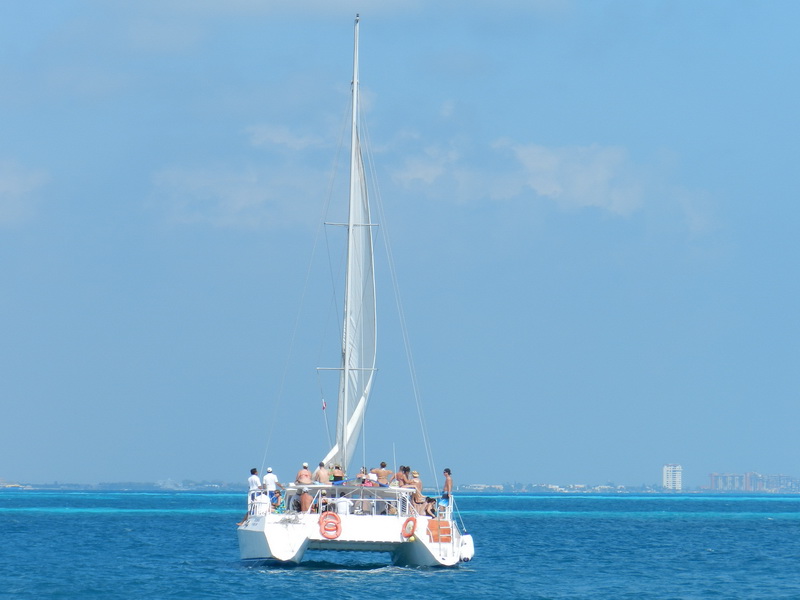 Catamaran Samba sailing with full mainsail on turquoise Caribbean Sea, Cancun hotel zone skyline visible in background sailing charter